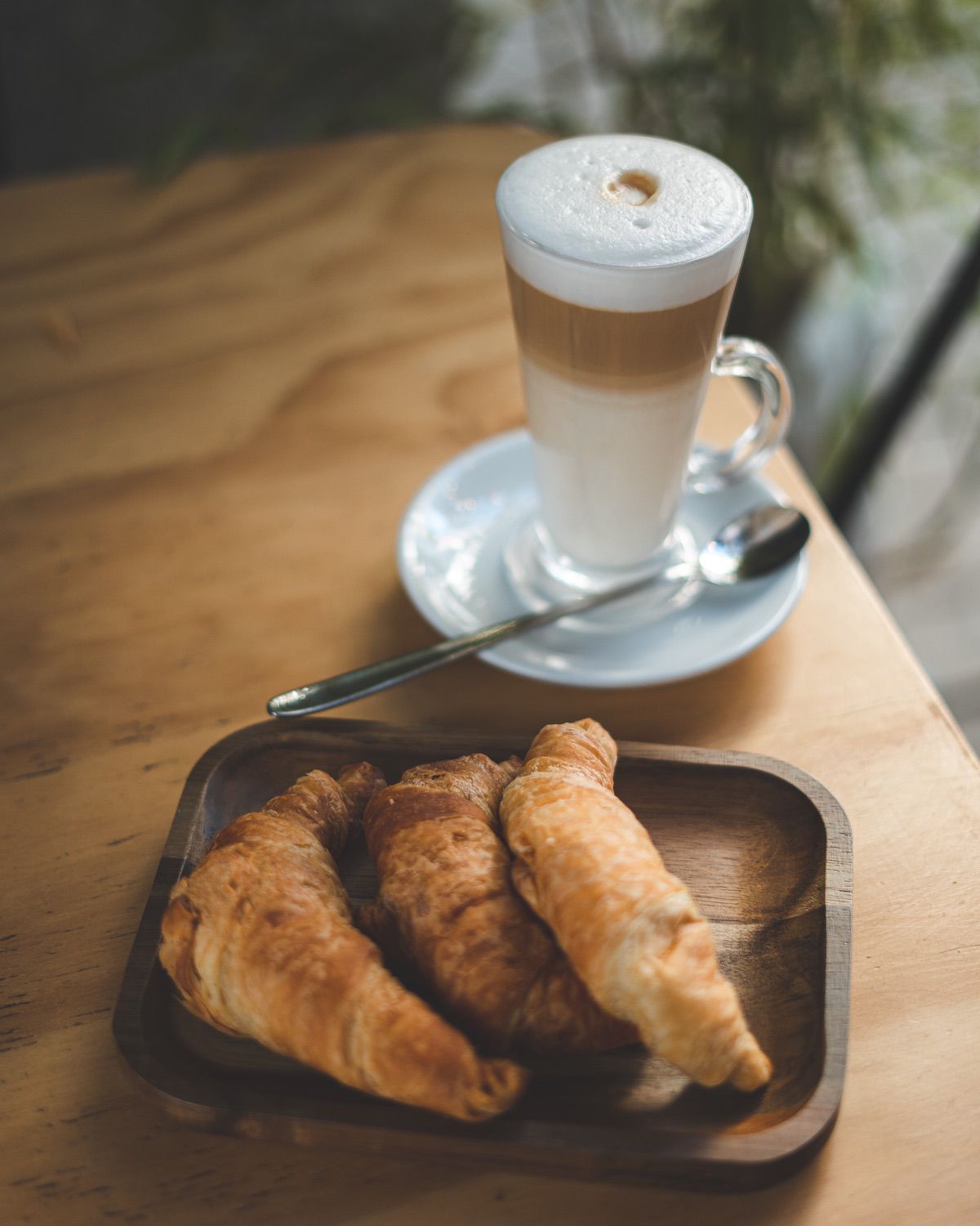 Taza de café con leche junto a dos croissants recién horneados sobre un plato