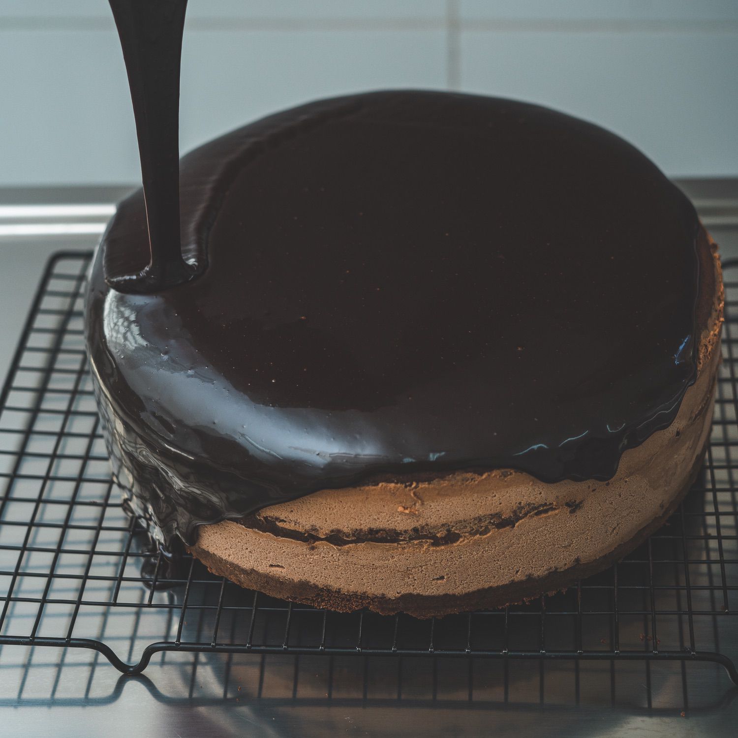 Manos cubriendo una torta con ganache de chocolate usando una espátula