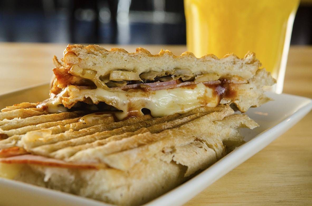 Panini de jamón y queso partido a la mitad, con el pan marcado por la plancha y el queso fundido saliendo por el corte